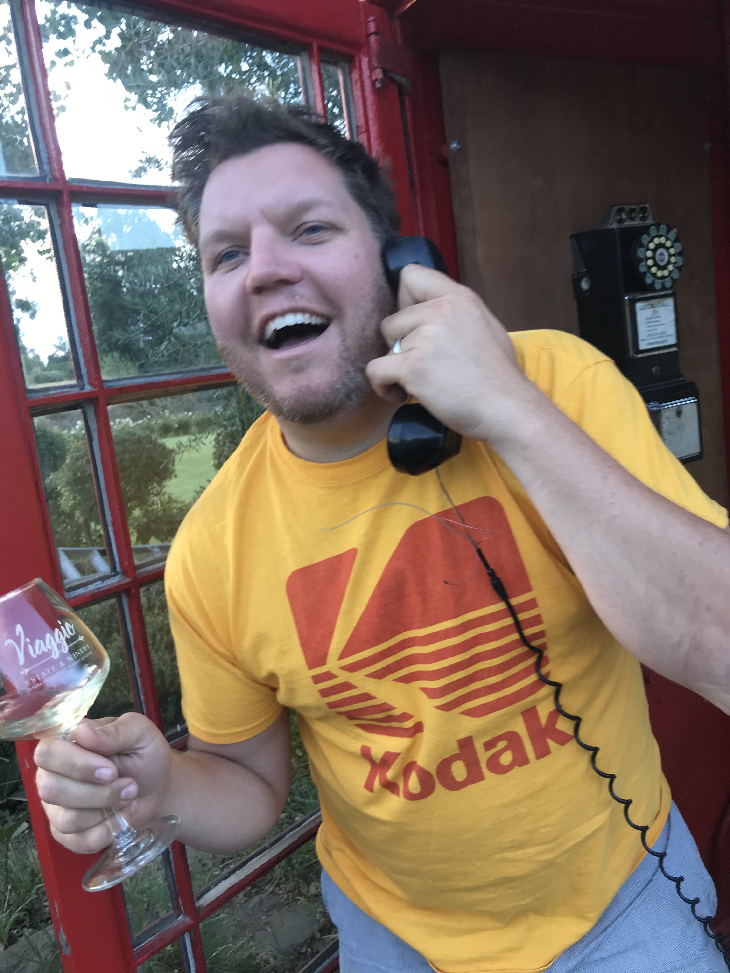 Matthew holding a glass of wine inside a red phone booth